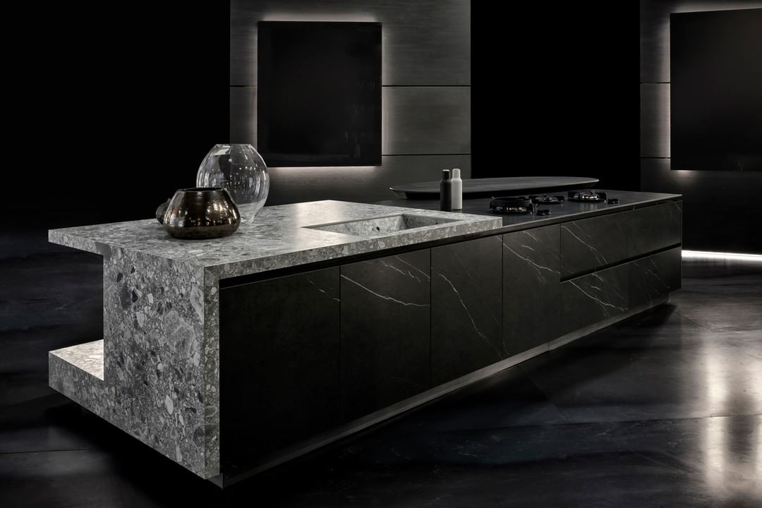 Dark designer kitchen with a thick grey granite island countertop and integrated stone sink